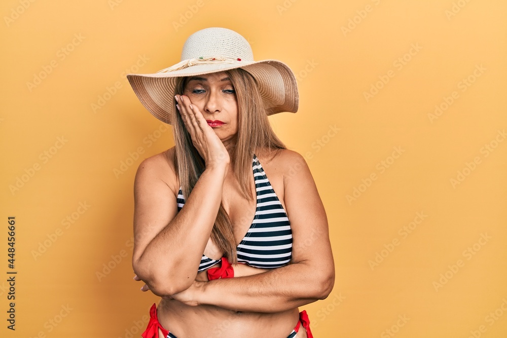 Middle age hispanic woman wearing bikini and summer hat thinking looking tired and bored with depression problems with crossed arms. Middle age hispanic woman wearing bikini and summer hat thinking looking tired and bored with depression problems with crossed arms.