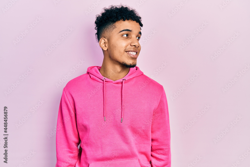 Young african american man wearing casual sweatshirt looking away to side with smile on face, natural expression. laughing confident. Young african american man wearing casual sweatshirt looking away to side with smile on face, natural expression. laughing confident.