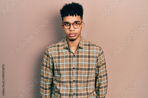 Young african american man wearing casual clothes and glasses with serious expression on face. simple and natural looking at the camera. © Krakenimages.com
