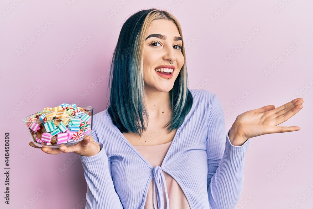 Young modern girl holding bowl of sugar candy celebrating achievement with happy smile and winner expression with raised hand Young modern girl holding bowl of sugar candy celebrating achievement with happy smile and winner expression with raised hand