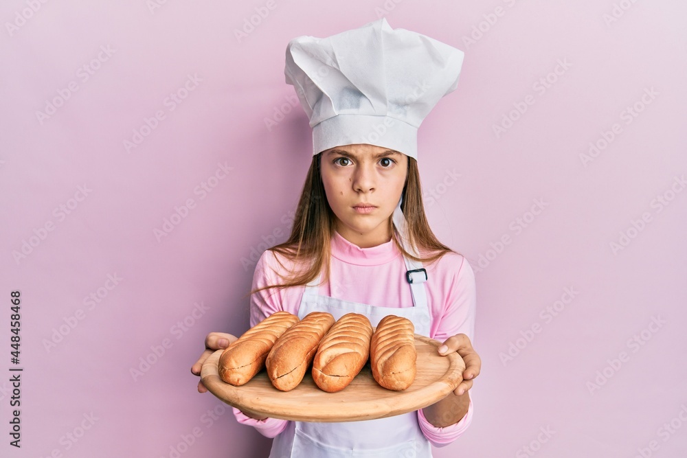 Beautiful brunette little girl wearing baker uniform holding homemade bread skeptic and nervous, frowning upset because of problem. negative person. Beautiful brunette little girl wearing baker uniform holding homemade bread skeptic and nervous, frowning upset because of problem. negative person.