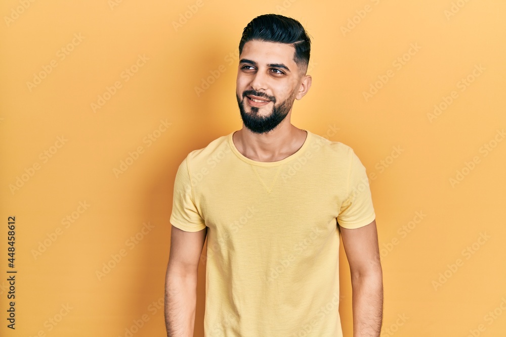 Handsome man with beard wearing casual yellow t shirt looking away to side with smile on face, natural expression. laughing confident. Handsome man with beard wearing casual yellow t shirt looking away to side with smile on face, natural expression. laughing confident.