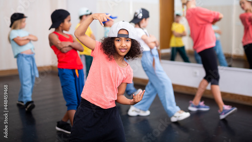Smiling curly preteen girl dancing hip hop during group dance class for children