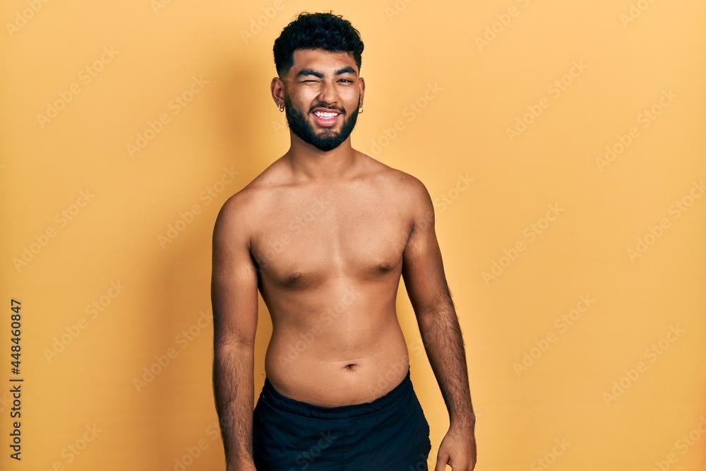 Arab man with beard wearing swimwear shirtless winking looking at the camera with sexy expression, cheerful and happy face.
