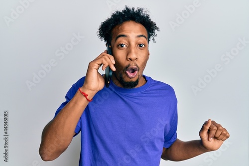 Young african american man with beard having conversation talking on the smartphone scared and amazed with open mouth for surprise  disbelief face