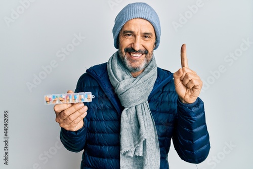 Middle age hispanic man holding pill organizer smiling with an idea or question pointing finger with happy face, number one photo