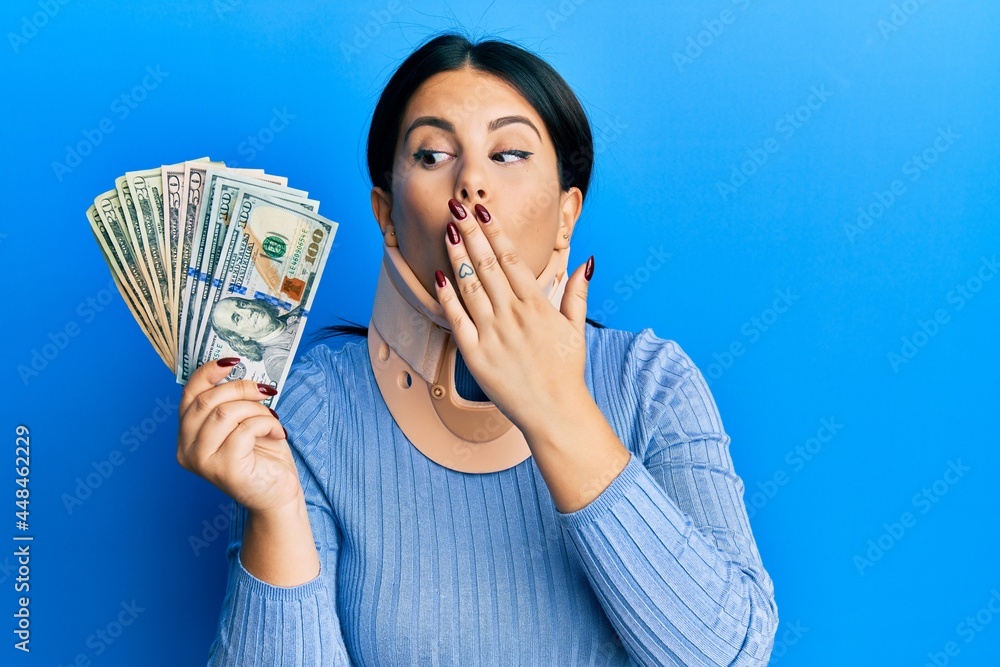 Beautiful brunette woman wearing cervical collar holding insurance money covering mouth with hand, shocked and afraid for mistake. surprised expression Beautiful brunette woman wearing cervical collar holding insurance money covering mouth with hand, shocked and afraid for mistake. surprised expression