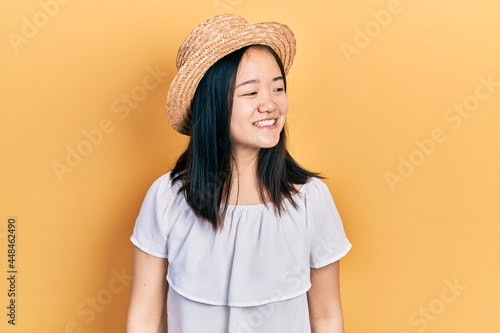 Young chinese girl wearing summer hat looking away to side with smile on face, natural expression. laughing confident.