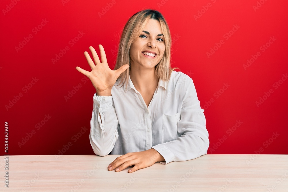 Young caucasian woman wearing casual clothes sitting on the table showing and pointing up with fingers number five while smiling confident and happy. Young caucasian woman wearing casual clothes sitting on the table showing and pointing up with fingers number five while smiling confident and happy.
