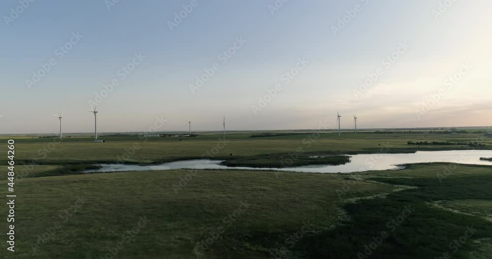 Aerial above green meadows and water pond towards highway and wind turbines. Sunset warm sky, South Dakota Aerial above green meadows and water pond towards highway and wind turbines. Sunset warm sky, South Dakota