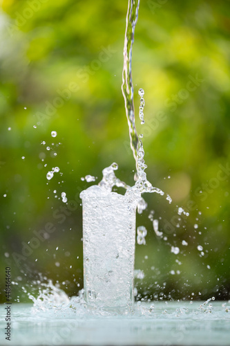 Drink water pouring in to glass over sunlight and natural green background.Water splash concept
