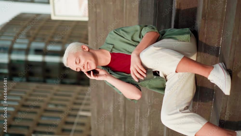 Zoom in slow motion vertical shot of young woman with short hair holding takeaway coffee cup sitting on steps and talking on cell phone. Happy female finishing call and thinking or day dreaming Zoom in slow motion vertical shot of young woman with short hair holding takeaway coffee cup sitting on steps and talking on cell phone. Happy female finishing call and thinking or day dreaming