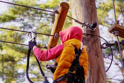 Brave kid in a high wire park above the ground. Ziplining. The child passes the rope obstacle course. back view