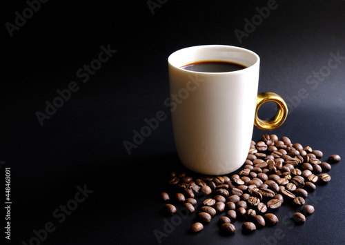 Welcome to the new morning aromatic and refreshing with a coffee mug white on a black background. There was brown coffee beans heap on the ground. 