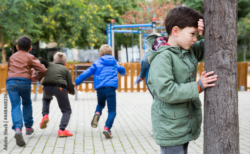Fototapeta premium Tween boy playing hide and seek with his friends on playground in autumn day..