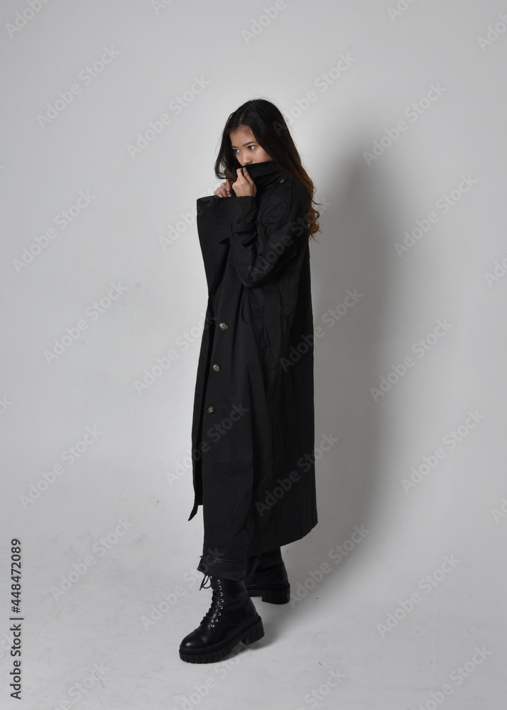 Full length portrait of pretty young asian girl wearing black tank top, utilitarian pants, leather boots and large dark coat. Standing pose with gestural hand movements, isolated on studio backgrou Full length portrait of pretty young asian girl wearing black tank top, utilitarian pants, leather boots and large dark coat. Standing pose with gestural hand movements, isolated on studio backgrou