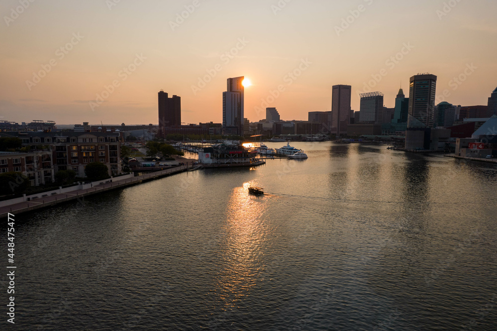 Aerial View of Baltimore City Inner Harbor at Sunset with Boat Passing in the Water Aerial View of Baltimore City Inner Harbor at Sunset with Boat Passing in the Water