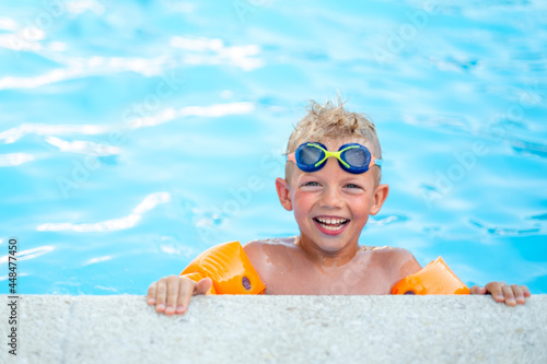 Portrait smiling boy in swimming pool, child in swimming glasses and inflatable sleeves. Summer travel hotel vacation or classes