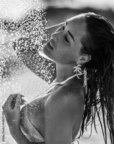 Portrait of sexy brunette woman in bikini taking shower on the beach, enjoys refreshing during vacation by the sea. Black and white. Summer vibes