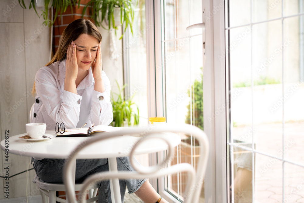 young tired woman in depression with a headache sits in a modern cafe holding her head with her hands. Joyless unmotivated employee at lunch in a restaurant. Spasm the head. young tired woman in depression with a headache sits in a modern cafe holding her head with her hands. Joyless unmotivated employee at lunch in a restaurant. Spasm the head.
