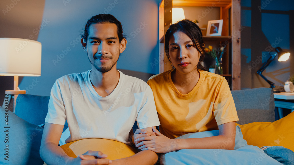 Φωτογραφία Happy young asia couple man and woman looking at camera smile and cheerful on video call online at night in living room at home, Stay at home quarantine, married life, Social distancing concept