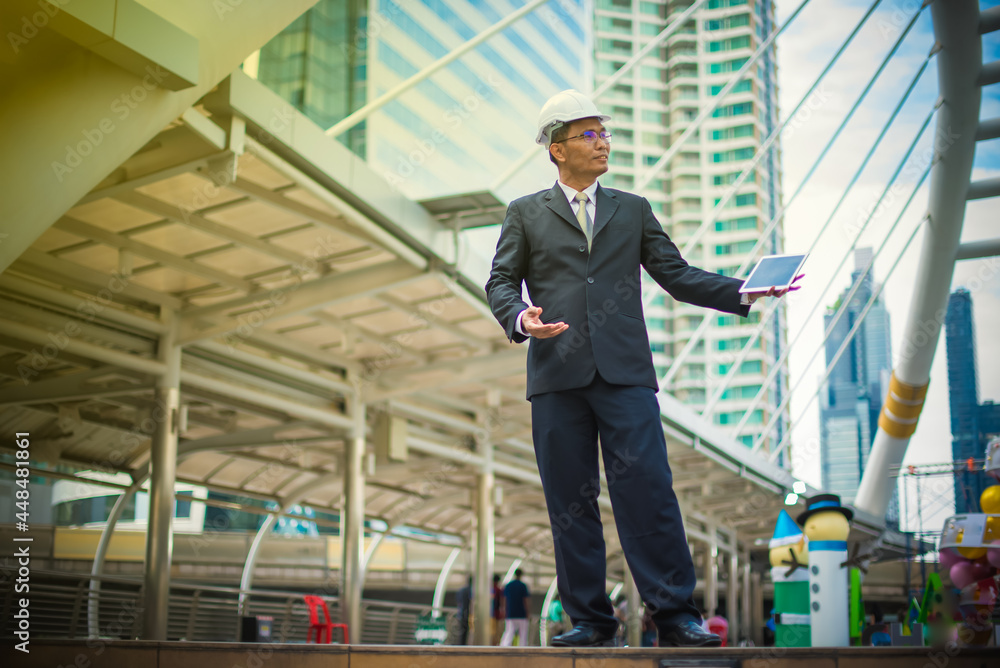 Businessman in black suit with white engineer helmet, Holding tablet and looking forward, Successful and Business Strategic planning concept-Image Businessman in black suit with white engineer helmet, Holding tablet and looking forward, Successful and Business Strategic planning concept-Image