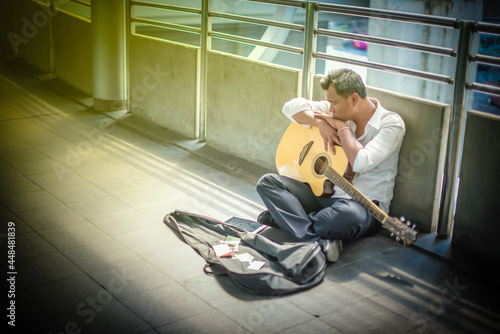 Unemployed man in white shirt, sitting a long the overpass feel very tired. He is falling a sleep with his guitar. The global economic crisis from COVID-19 concept.