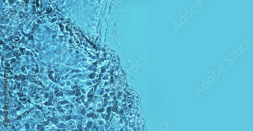 Transparent blue water surface with ripples and splashes. Summer water waves background in sunlight. copy space