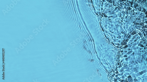 Transparent blue water surface with ripples and splashes. Summer water waves background in sunlight. copy space