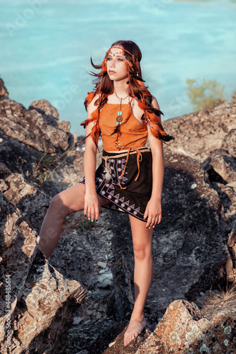 A young girl in an Indian outfit stands on the top of a mountain and looks into the distance