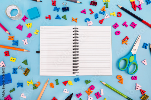 white blank notebook and miscellaneous school supplies on a blue background. School concept.