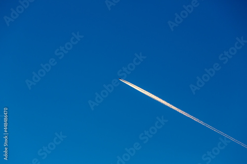 Condensation light line in the sky from aircraft. Trail of the plane on blue background. Airplane with white trace in clear sky. he line on sky look like plane crash comet and meteor.