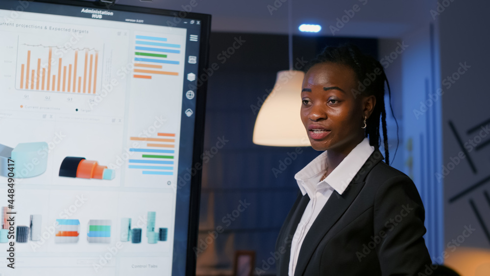 African american executive manager standing in front of presentation monitor analyzing marketing statistics late at night in meeting room. Diverse multi ethnic teamwork brainstorming business ideas African american executive manager standing in front of presentation monitor analyzing marketing statistics late at night in meeting room. Diverse multi ethnic teamwork brainstorming business ideas