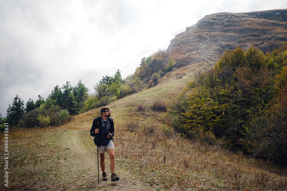 man with backpack and sticks for trekking hiking in the mountains. The beginning of autumn season. Beautiful foggy weather