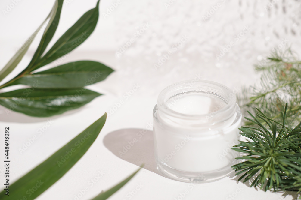 natural moisturizing fase cream on white table next to green leaves and branches. eco cosmetics concept. face care and nourishing. unbranded white bottle of cream natural moisturizing fase cream on white table next to green leaves and branches. eco cosmetics concept. face care and nourishing. unbranded white bottle of cream