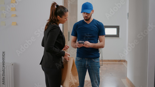 Businesswomn working in startup company office receiving takeaway food meal box paying order with smartwatch using POS service. Delivery guy worker delivering lunch purchase during lunchtime photo