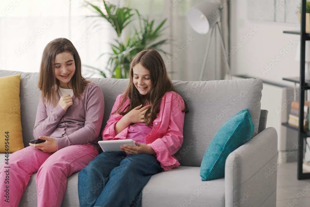 Happy girls sitting on the sofa and connecting with a digital tablet Happy girls sitting on the sofa and connecting with a digital tablet
