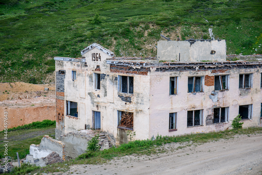 A destroyed administrative multi-storey brick building in a mountain valley. Summer landscape in the Altai Republic in Russia. Remains of a mine for the extraction of minerals.