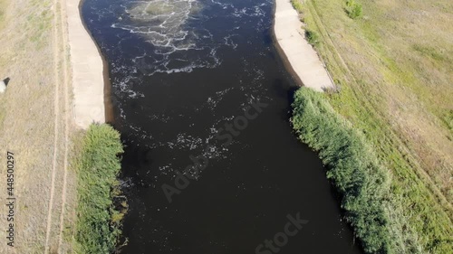 Aerial of an irrigation field canal constructed to convey water. Day drone view of Saratov area in Russia, around a field with green trees next to a dirt road.