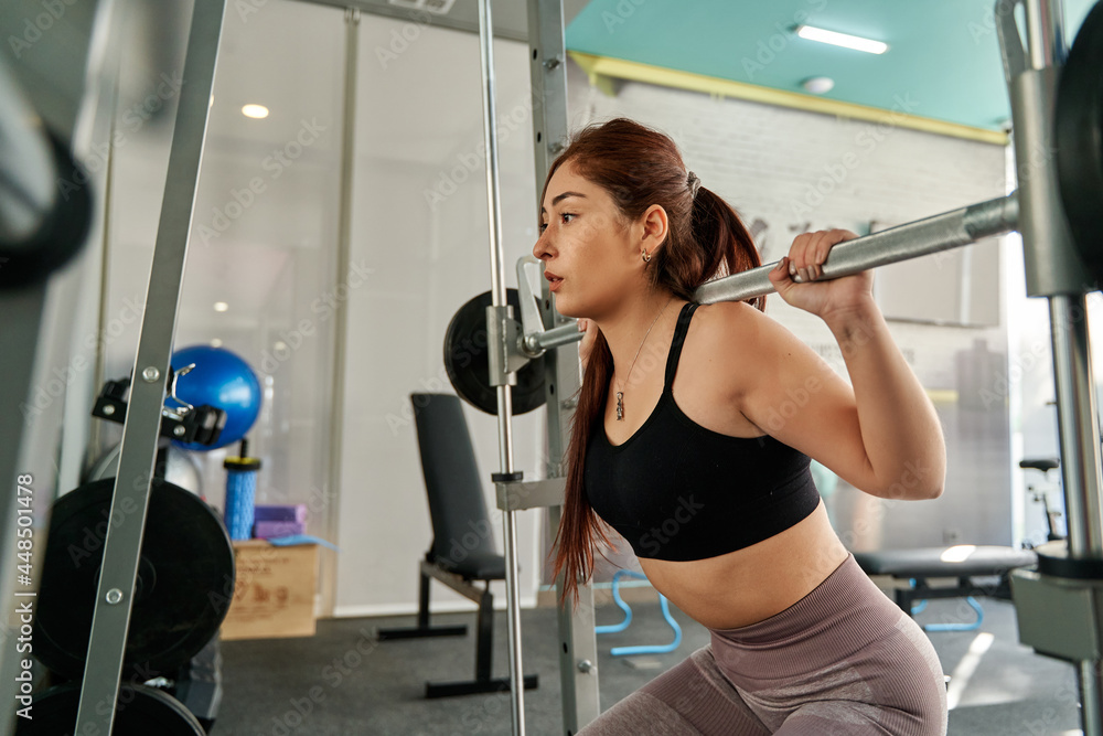 Fototapeta premium young redheaded woman performing a squat on a smith machine