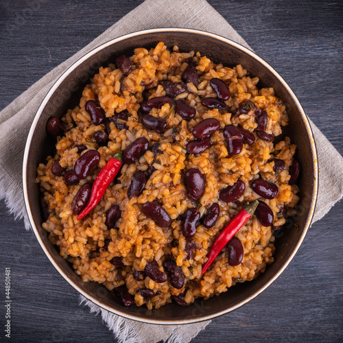 Mexican tomato rice with beans in a plate on a dark table with hot peppers, top view, close-up