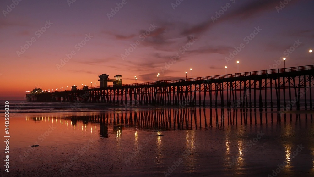Pier silhouette Oceanside California USA. Pacific ocean tide tropical beach. Summertime gloaming atmosphere. Purple aesthetic gradient, calm twilight sky, pink violet dusk. Lights reflection in water. Pier silhouette Oceanside California USA. Pacific ocean tide tropical beach. Summertime gloaming atmosphere. Purple aesthetic gradient, calm twilight sky, pink violet dusk. Lights reflection in water.