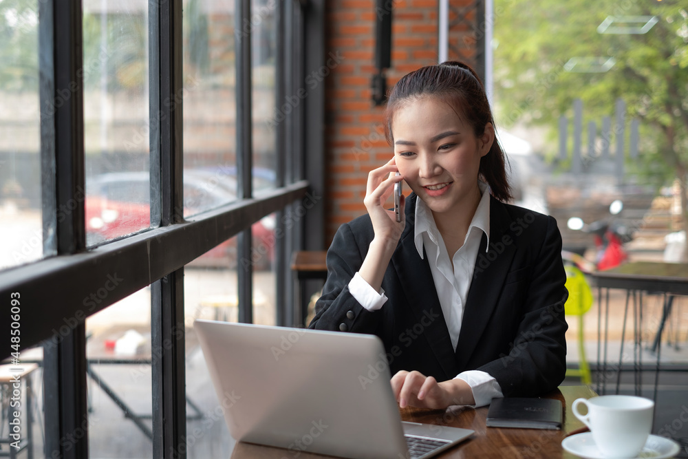 Young Asian businesswoman talking on the phone using a laptop keyboard at the office. Young Asian businesswoman talking on the phone using a laptop keyboard at the office.