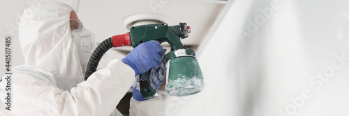 Construction worker in protective suit and respirator painting wall with spray gun