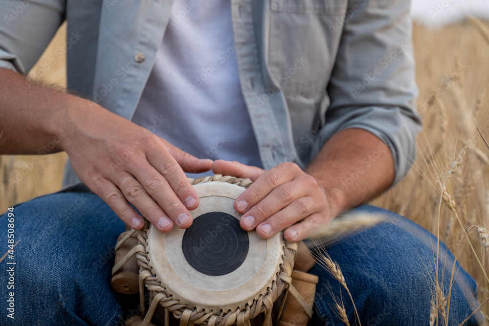 Close-up of a man playing a djembe sitting in a wheat field Close-up of a man playing a djembe sitting in a wheat field