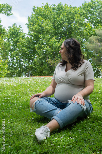 Pregnant woman sitting on the grass and posing happily