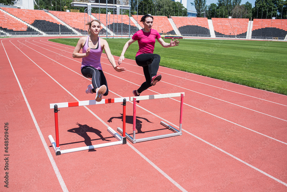 Fototapeta premium Two female sportswomen are jumping over an obstacle. Running with hurdles. Active lifestyle