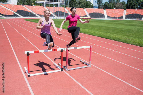 Two female sportswomen are jumping over an obstacle. Running with hurdles. Active lifestyle
