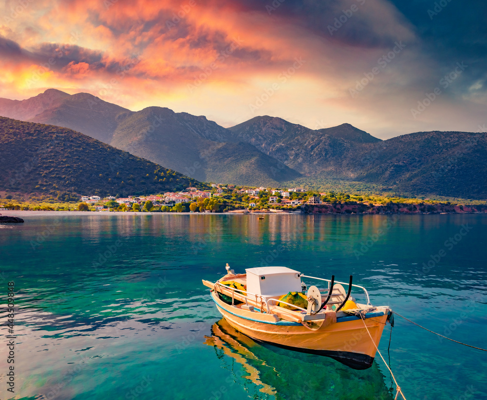 Colorful sunrise in Logari port with small fishing boat with Kyparissi village on background. Picturesque summer scene of Peloponnese peninsula, Greece, Europe. Calm morning seascape of Myrtoan Sea.