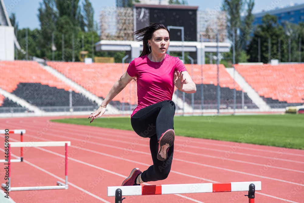 Woman athlete jumping over an obstacle. Running with hurdles. Active lifestyle